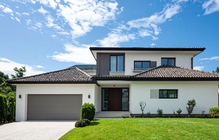 Maison moderne avec façade en bois et verre, éclairage extérieur, ciel nuageux.