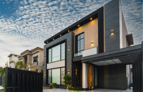 Maison moderne avec façade en bois et verre, éclairage extérieur, ciel nuageux.
