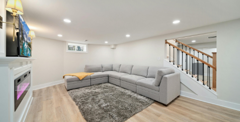 Extension : Aménagement sous-sol ou garage Aménagement d'un sous-sol Canapé gris en un salon clair avec un tapis et un escalier en bois à l'arrière.